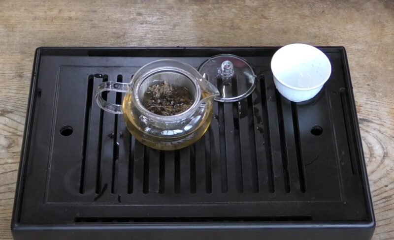 Glass teapot with a strainer on a black tray